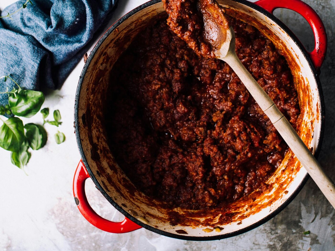 Panela de ferro vermelha cheia de carne moída refogada, com colher de pau