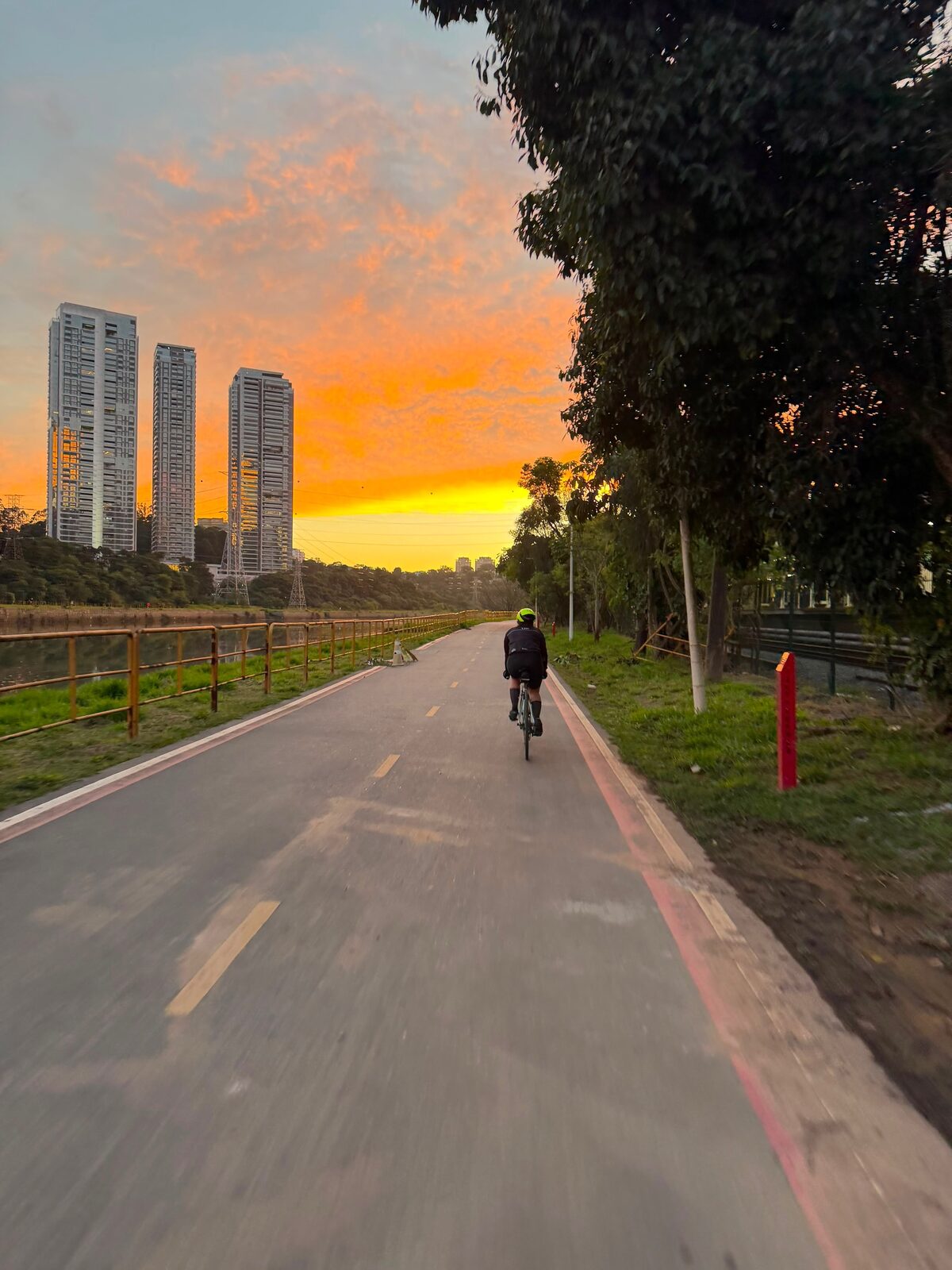 Ciclista pedalando sozinho numa ciclovia de São Paulo no fim da tarde, com o céu laranja